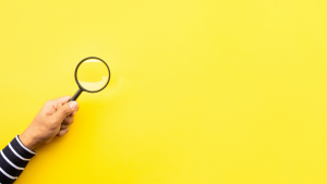 Person holding a magnifying glass against a yellow backgroud