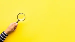 Person holding a magnifying glass against a yellow backgroud