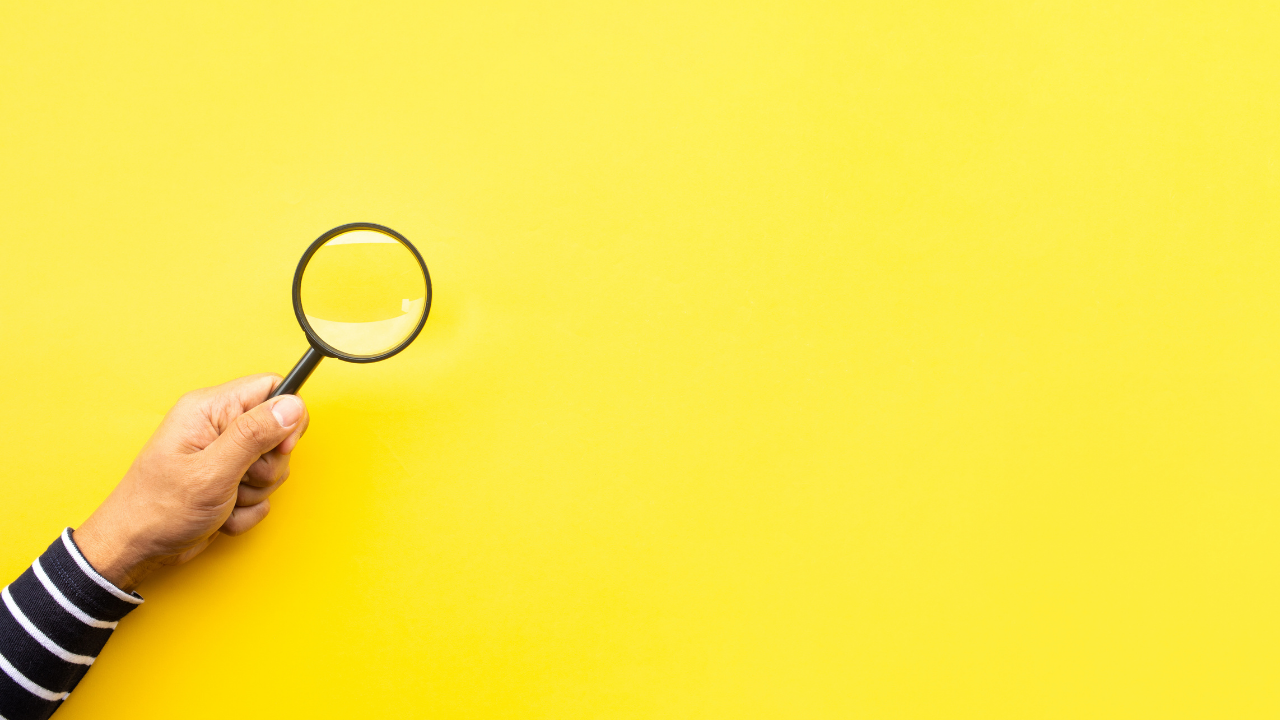 Person holding a magnifying glass against a yellow backgroud