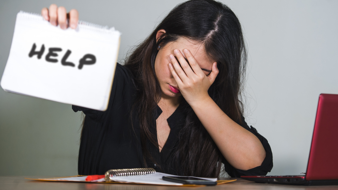 Woman with head in hands holding up a help sign